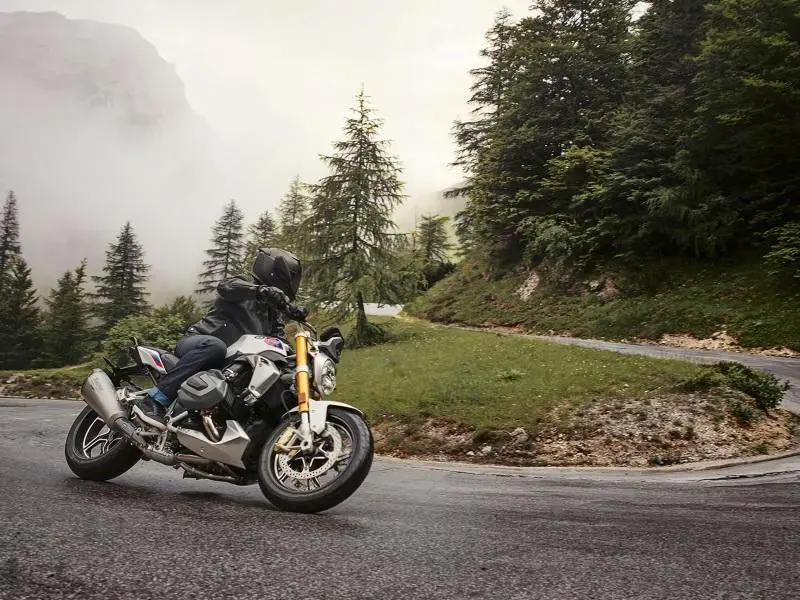 Person riding a 2020 BMW R 1250 R motorcycle down a winding road.